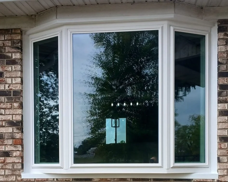 Bay window on brick house exterior reflecting trees and basketball hoop.